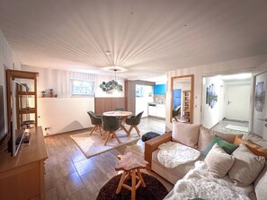 Ein modernes Wohnzimmer mit Essbereich, einer Küche im Hintergrund und einem großen Spiegel, der den Raum widerspiegelt.