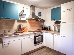 Eine moderne Küche mit weißen Schränken, einer Edelstahlspüle, einem eingebauten Backofen und einer Kaffeemaschine.