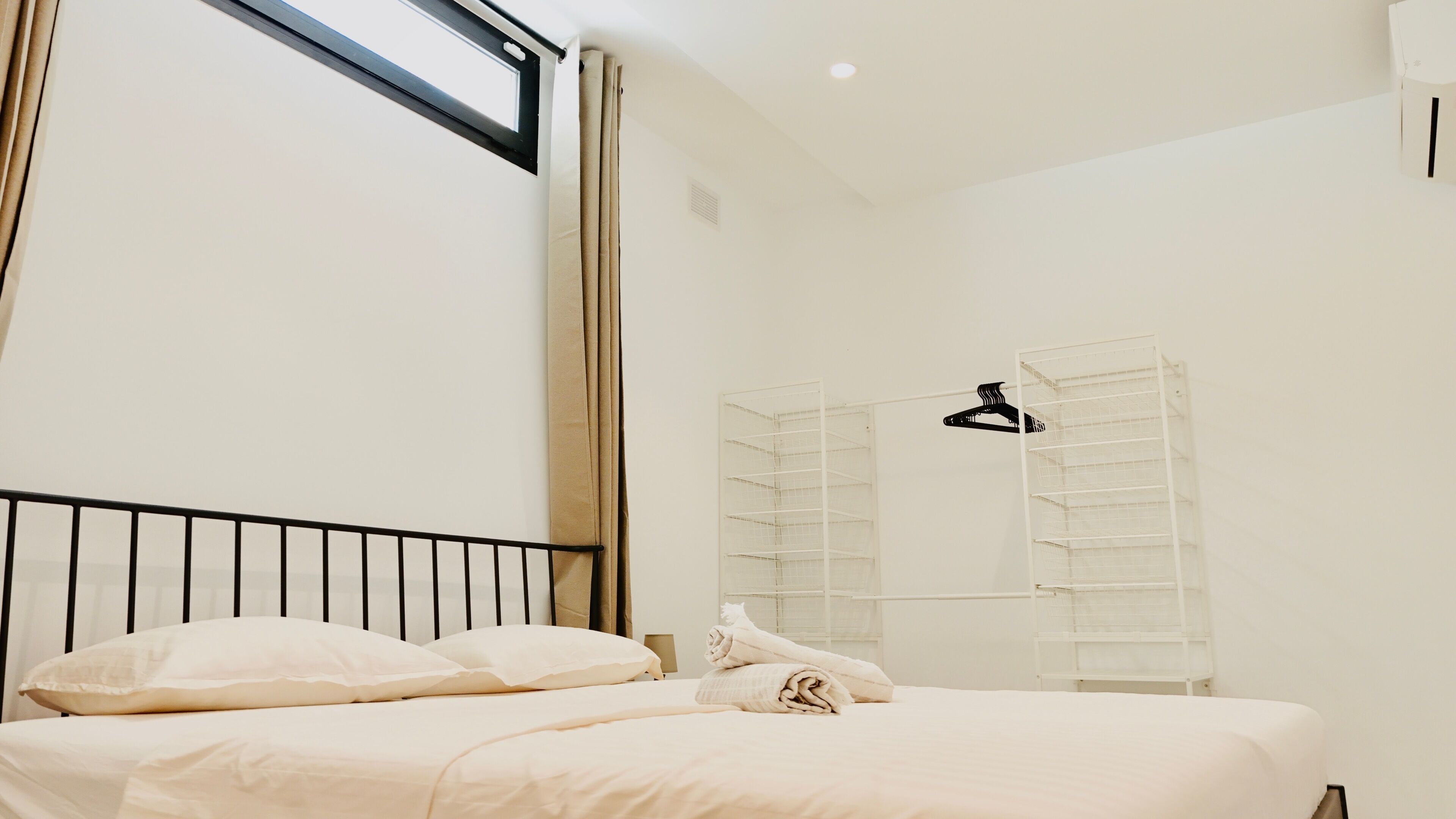 A bedroom with a bed, a window, a wardrobe, and a hanging rack.