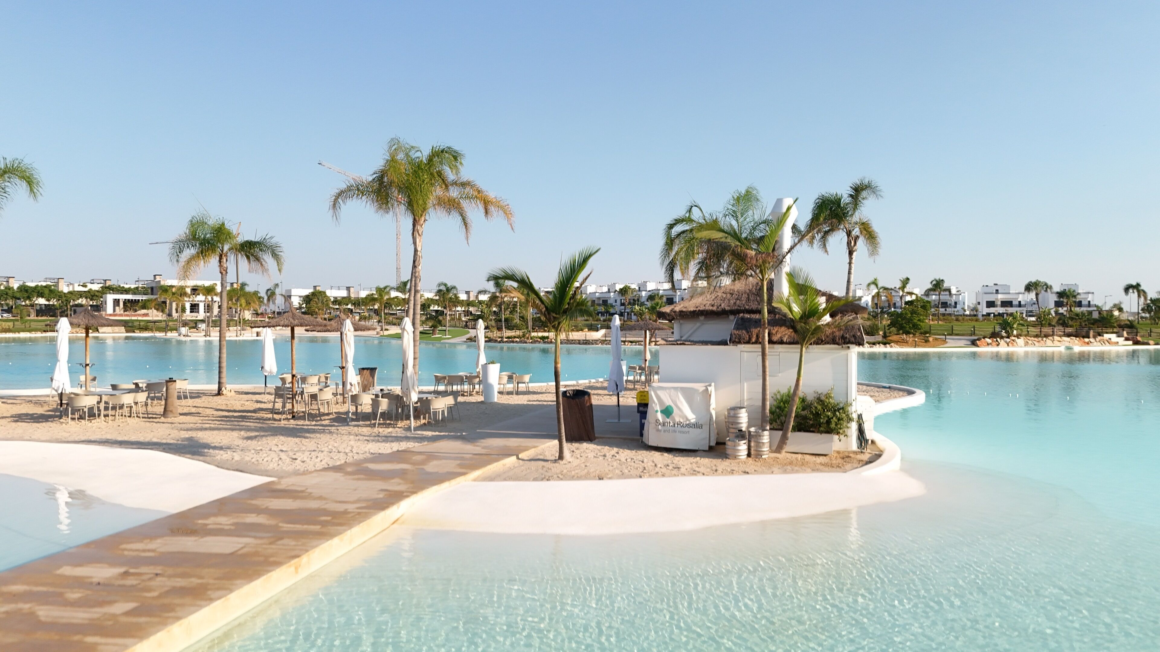 Área de piscina em resort, com espreguiçadeiras, guarda-sóis e palmeiras.