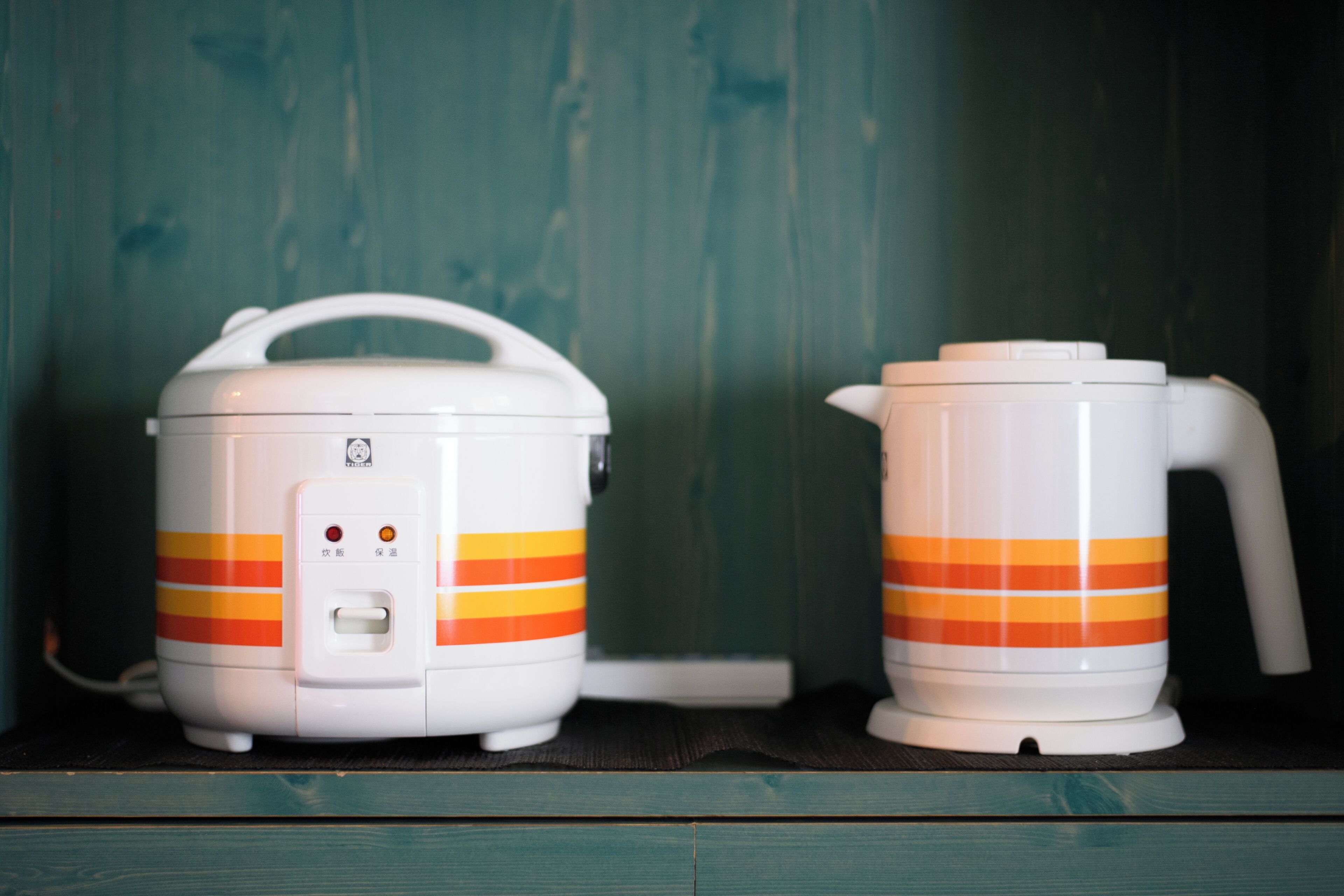 Two white appliances with orange stripes, a handle, and a control panel, placed on a shelf against a wooden background.