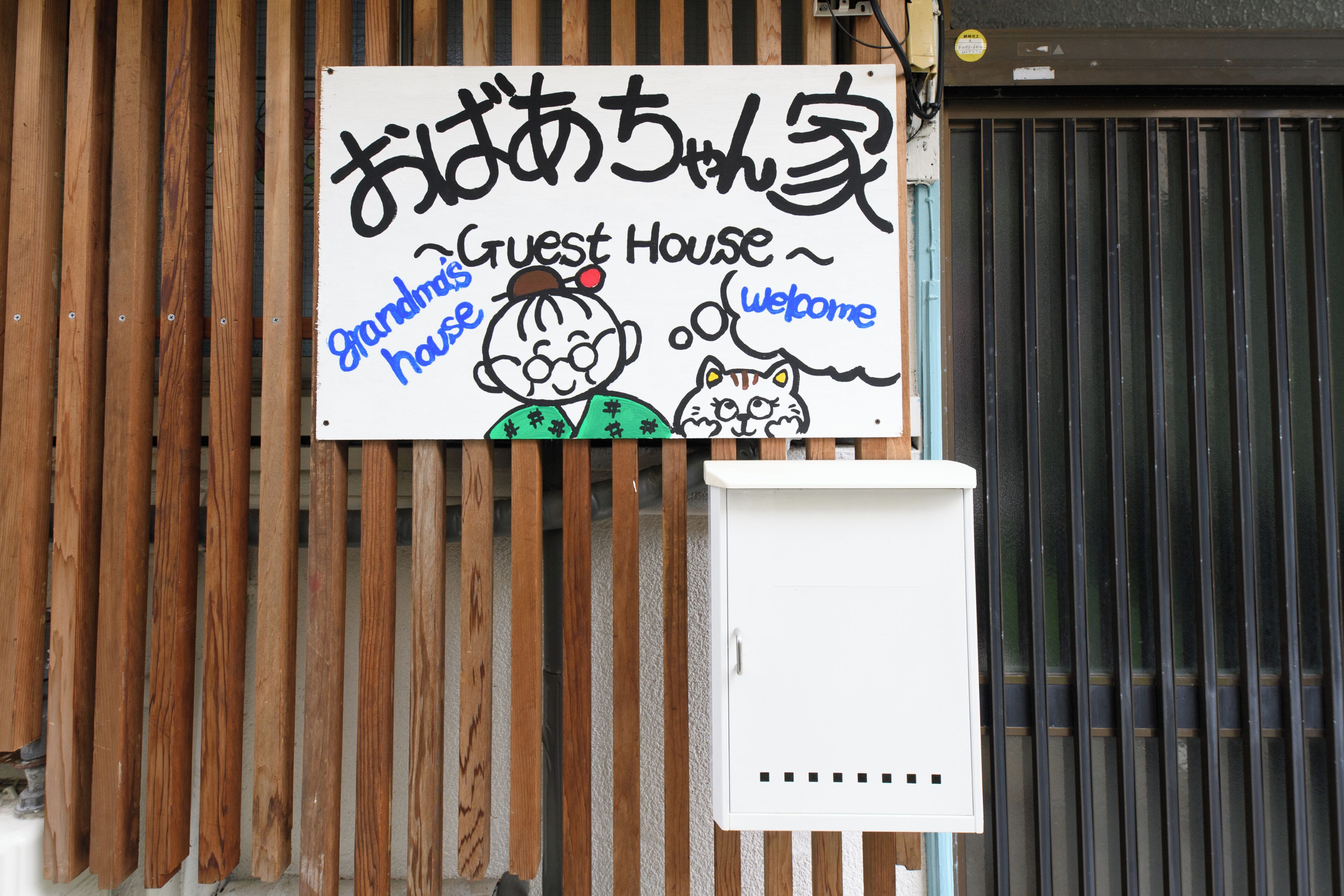 A sign with Japanese characters and a cartoon character welcoming guests to a 'Grandma's House' guest house.