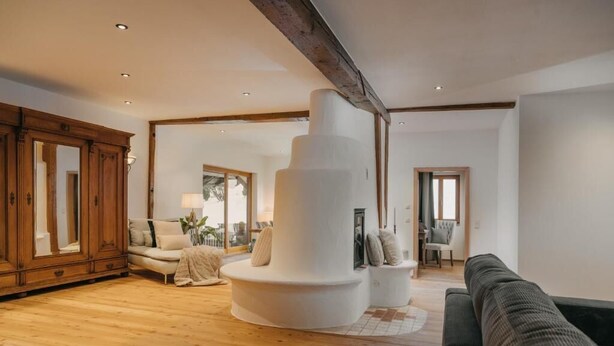 A spacious living room with a wooden floor, a large white circular structure, a dark green sofa, and a wooden cabinet. - Mika Hof exklusive Apartments (Weitnau)