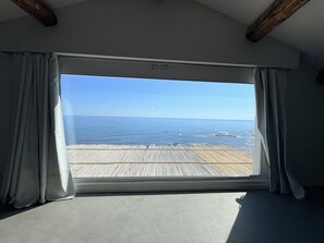 Een kamer met een groot raam, houten balken in het plafond en uitzicht op zee.