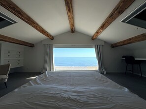 Een slaapkamer met een groot bed, een bureau, een stoel en uitzicht op zee.