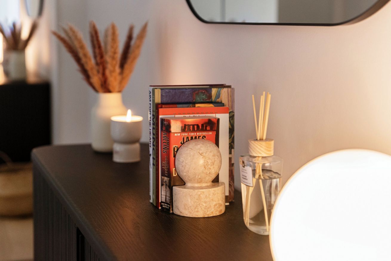 A bookshelf with books, a candle, and a decorative item on a dark wooden surface.
