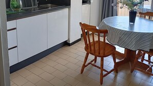 Eine kompakte Küche mit weißen Schränken, einer schwarzen Arbeitsplatte und einem Essbereich mit rundem Tisch und Holzstühlen.