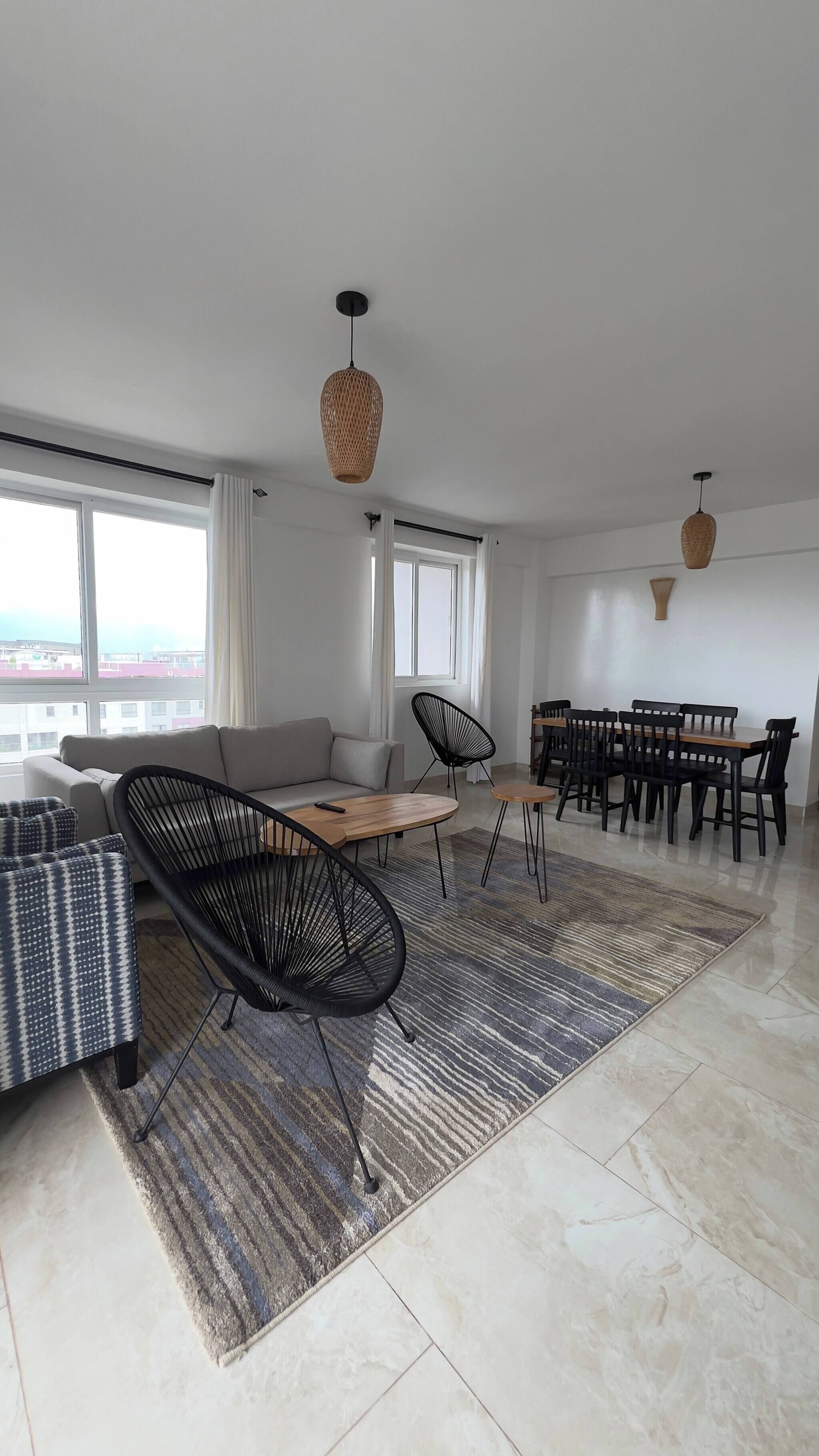 A modern living room with a sofa, chairs, a dining table, and large windows.