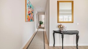 A hallway with a rug, a painting, a mirror, and a console table with flowers. - Luxury Sunbury retreat (Sunbury)
