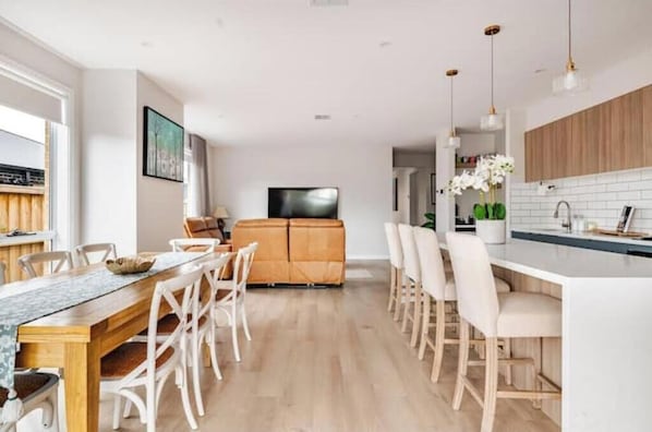 Una cocina moderna con una isla central, armarios de madera y un comedor con sillas blancas.