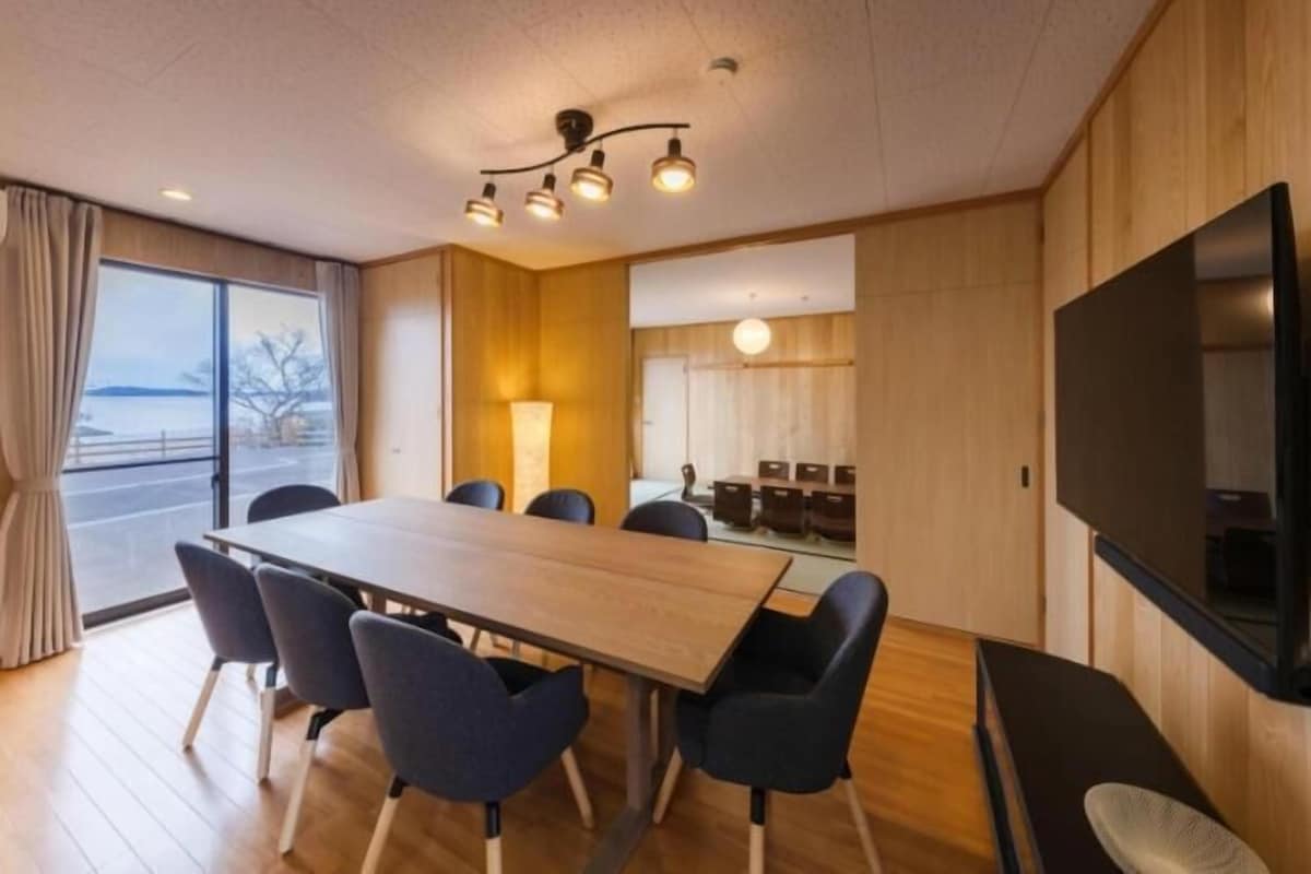 A conference room with a long table, chairs, a TV, and a large window.