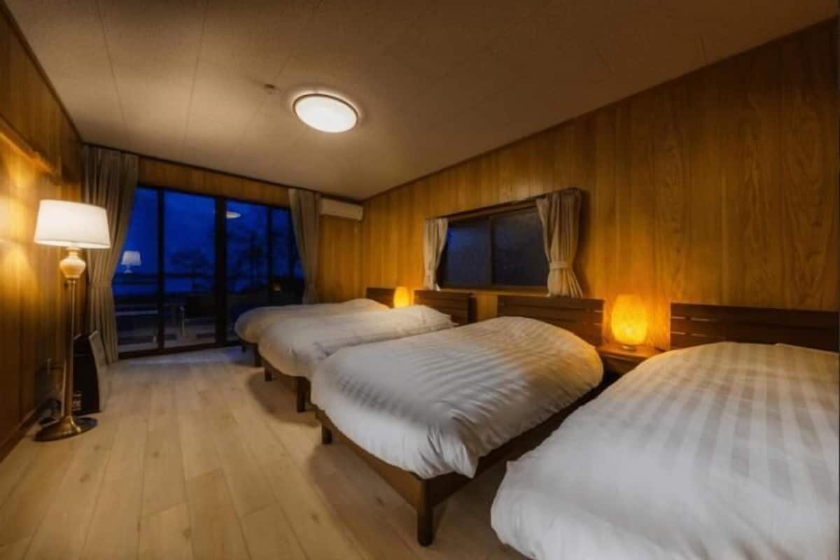 Habitación de hotel con tres camas, piso de madera, un ventanal grande y una lámpara en el techo.