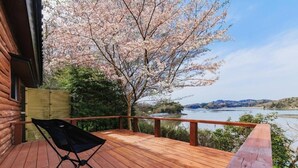 A wooden deck with a folding chair, overlooking a river and hills.