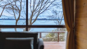 A room with a view of a body of water and trees through a window.
