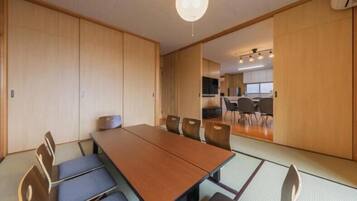 A conference room with a long table and chairs, wooden sliding doors, and a kitchen area in the background.
