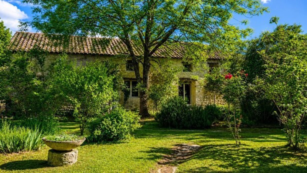 Une maison en pierre avec un toit de tuiles, entourée d’une végétation luxuriante et d’un jardin bien entretenu.