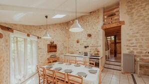 Un espace repas avec un mur en pierre, des meubles en bois et une cuisine en arrière-plan.