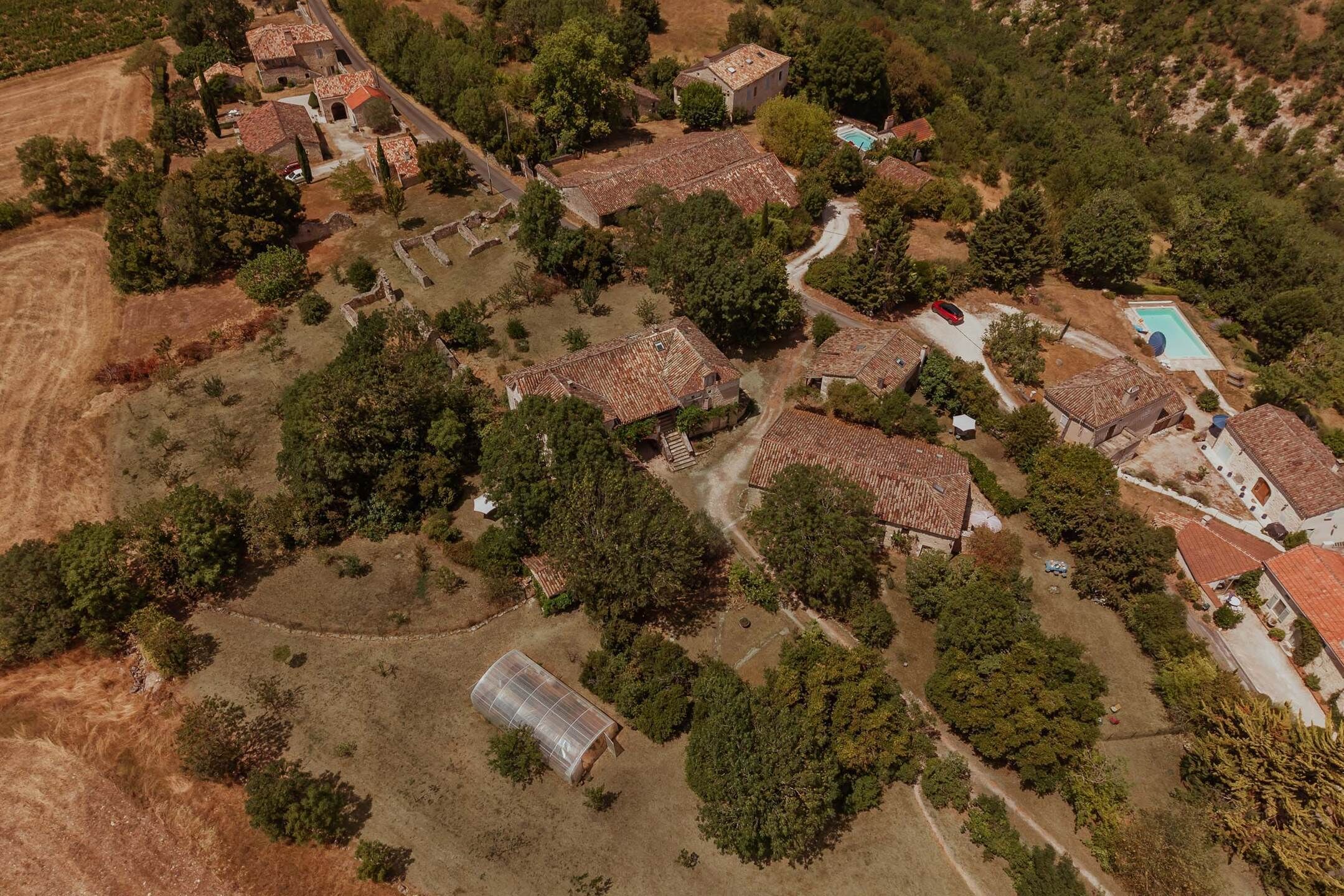An aerial view of a residential area with multiple houses, a swimming pool, and a greenhouse.