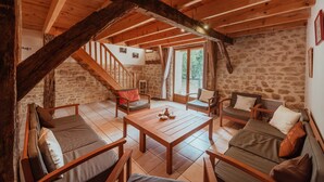 Un intérieur rustique avec un plafond en bois, des murs en pierre, un escalier et un coin salon avec une table.