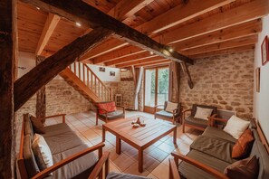 A rustic interior with a wooden ceiling, stone walls, a staircase, and a seating area with a table. - Gite authentique de charme Rocamadour (Trespoux-Rassiels)