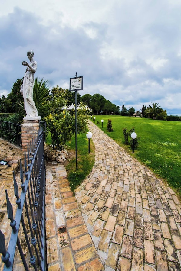 A paved pathway leading to a statue, with a sign reading 'Cagli Neelli.'