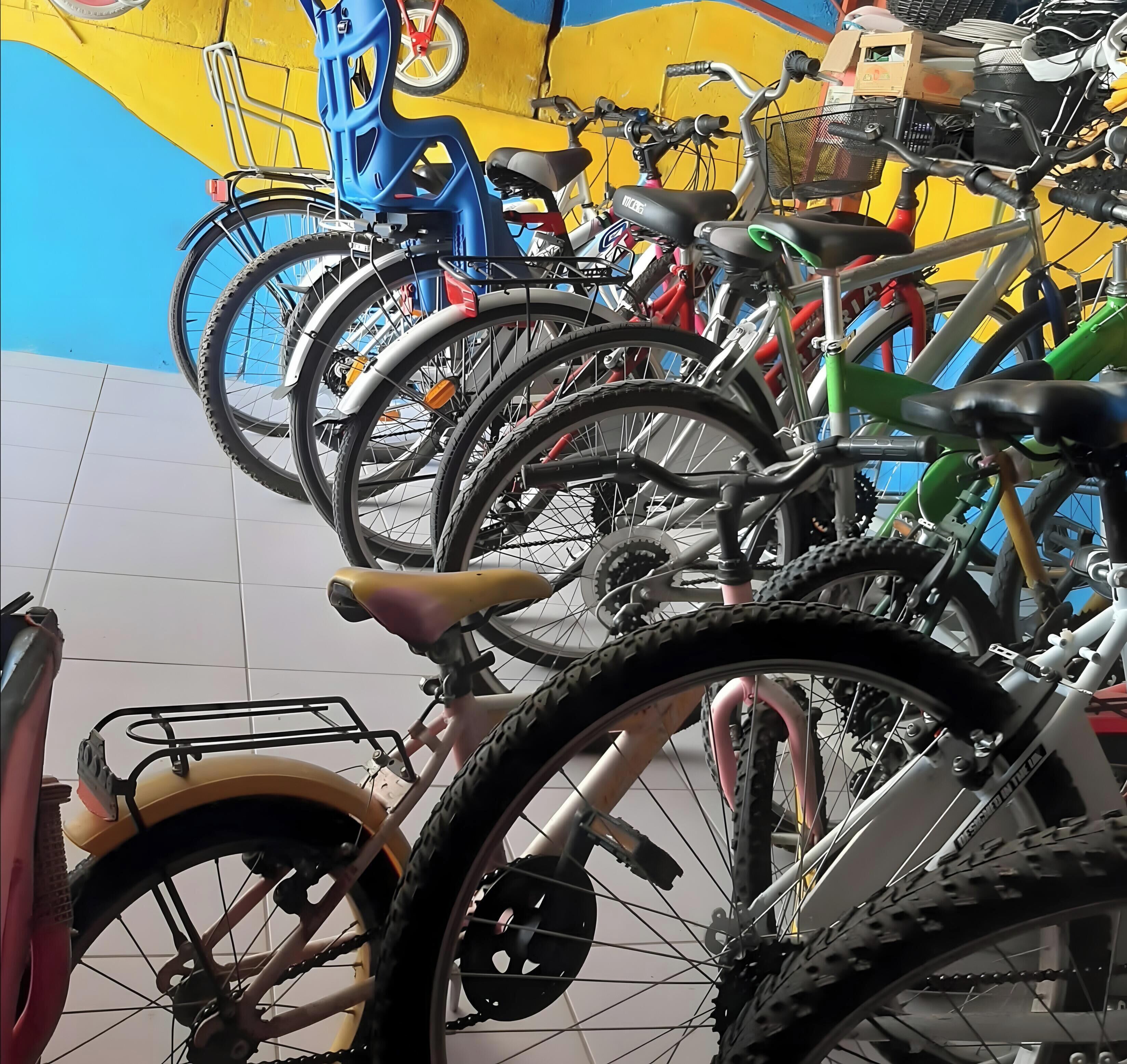 Una fila de bicicletas estacionadas en un espacio interior, con piso de baldosas y una pared colorida al fondo.