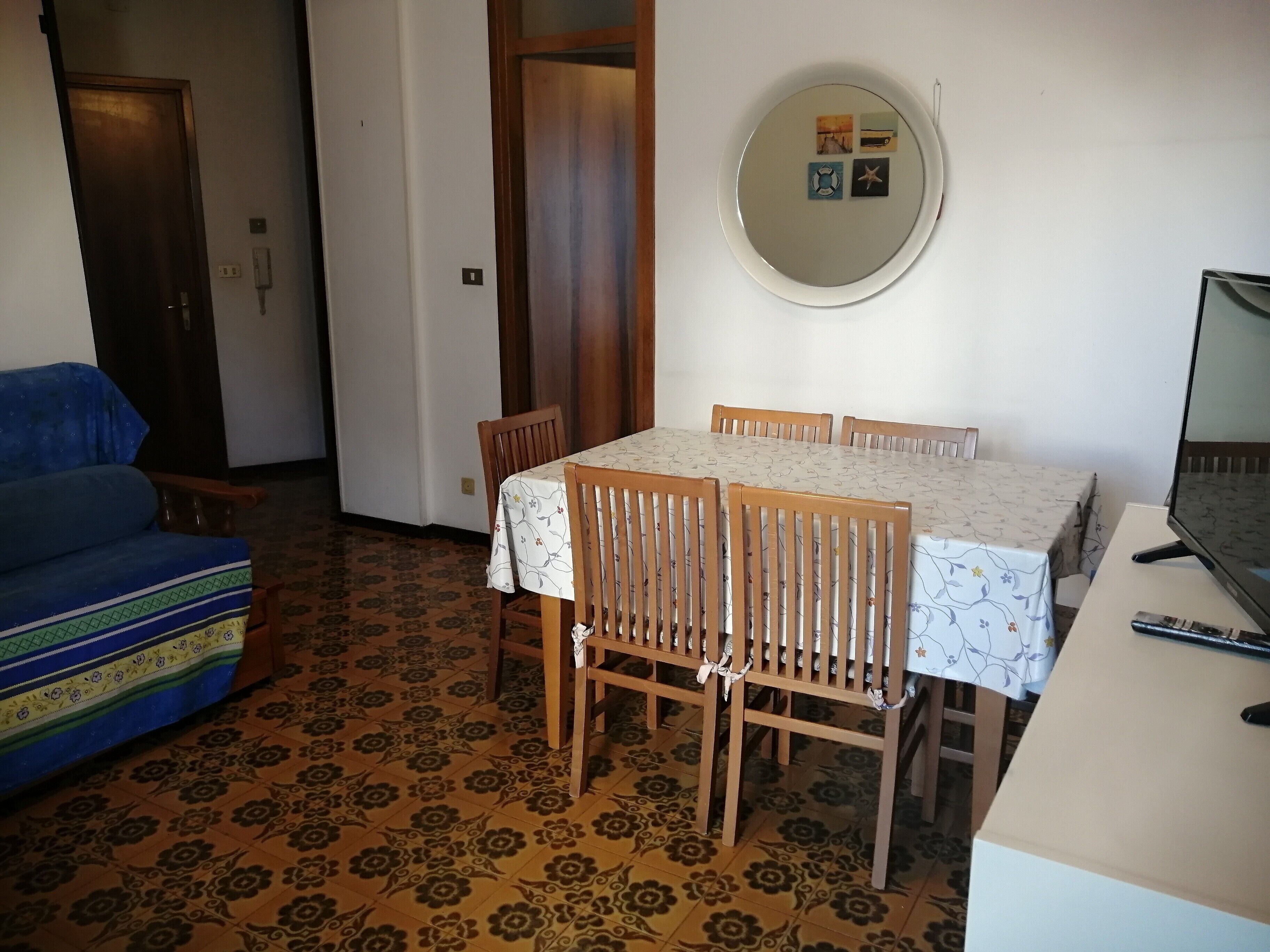 A dining area with a table, chairs, a television, and a patterned floor.