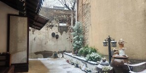 A courtyard with a brick wall, potted plants, a lantern, and a large pot. - Hanok1942 (Daegu)