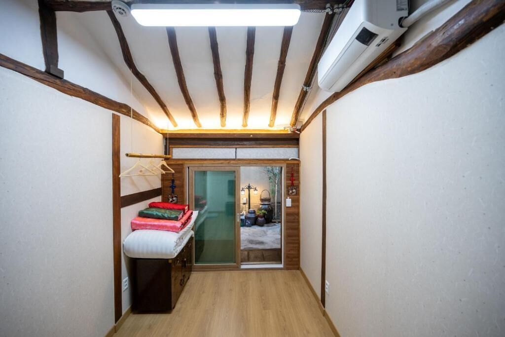 Un pasillo estrecho con vigas de madera, una cama con almohadones, un perchero y una puerta corrediza de vidrio que da a un espacio al aire libre.