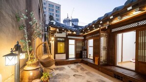 Ein traditioneller japanischer Innenhof mit Tatami-Matten, Holzbauten und Blick auf moderne Gebäude im Hintergrund.