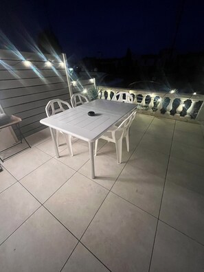 Eine Terrassengruppe draußen mit weißem Tisch und Stühlen, umgeben von einem Geländer mit Beleuchtung.