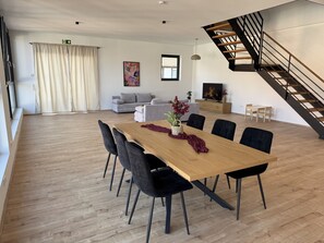 Ein großzügiger Wohnbereich mit einem Holzesstisch, schwarzen Stühlen, einem grauen Sofa, einer Treppe und einem Fernseher.