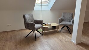 Ein modernes Schlafzimmer im Loft-Stil mit Dachfenster, zwei Polstersesseln, einem kleinen Holztisch und einer Stehlampe.