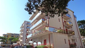 A multi-story building with balconies, a parking area, and a tree in the foreground. - Apartment 'Acapulco Residence 201' with Shared Pool and Private Terrace (Lido di Jesolo)