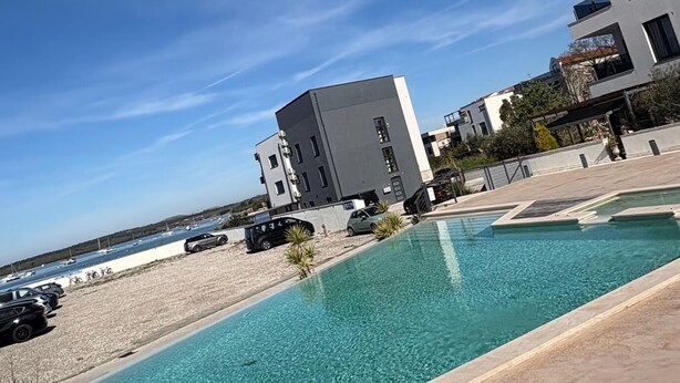Una piscina con cielo azzurro limpido, edifici moderni e un'area parcheggio.