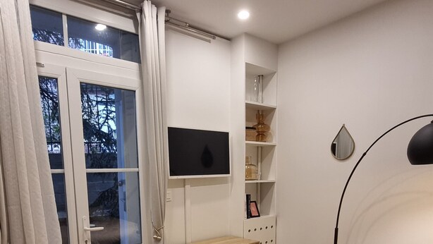 A bedroom with a bed, a desk with a TV, a lamp, and a window with curtains.