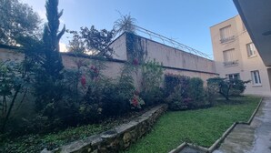 A courtyard with a stone wall, greenery, and a building with balconies.