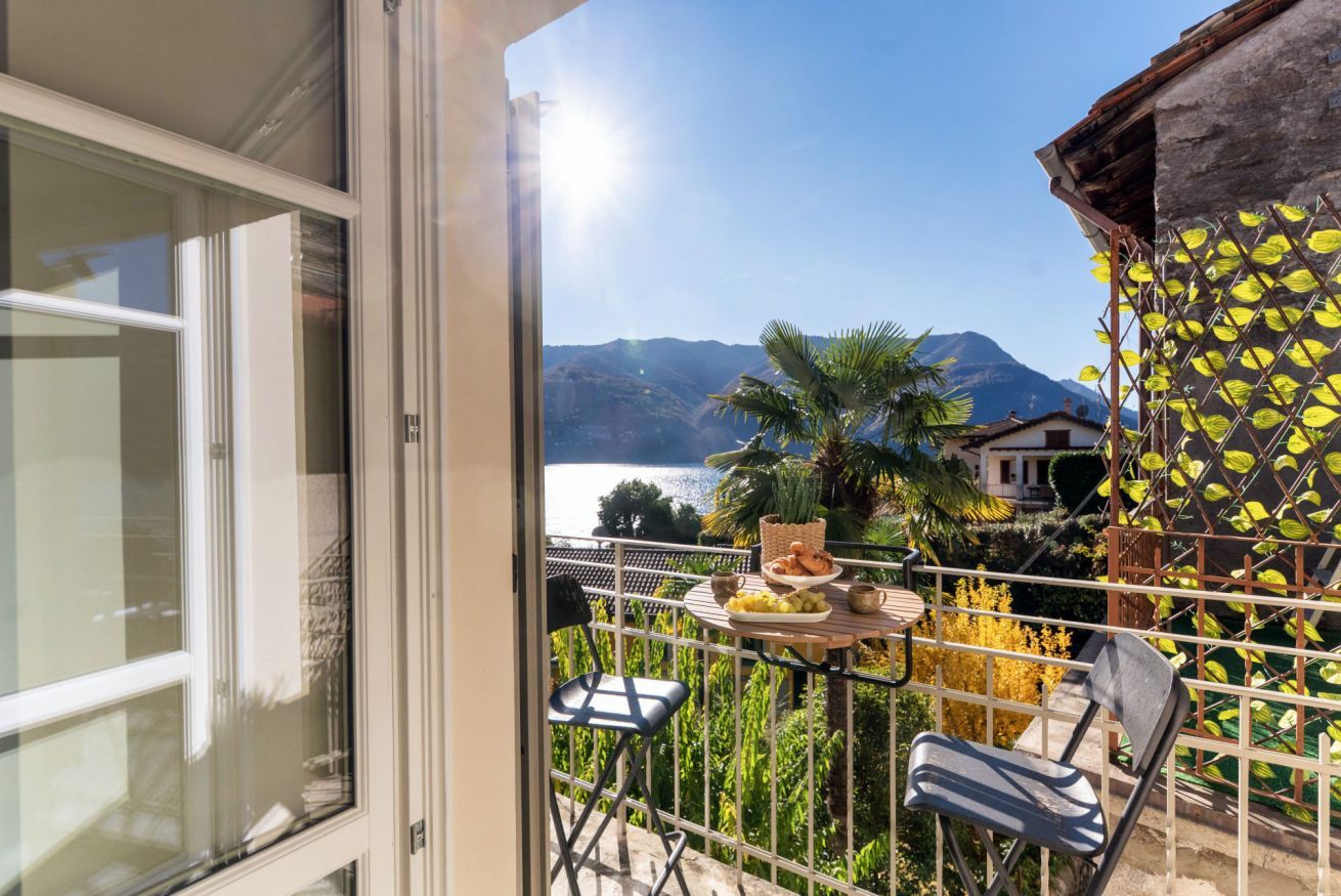A balcony with a table set for breakfast, a chair, and a view of mountains and a lake.