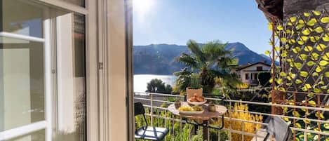 A balcony with a table set for breakfast, a chair, and a view of mountains and a lake.
