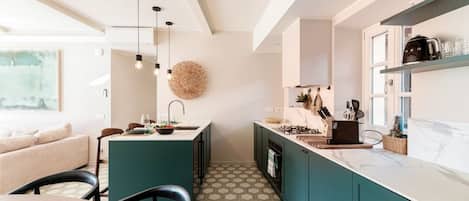 A modern kitchen with teal cabinets, a marble countertop, and pendant lighting.