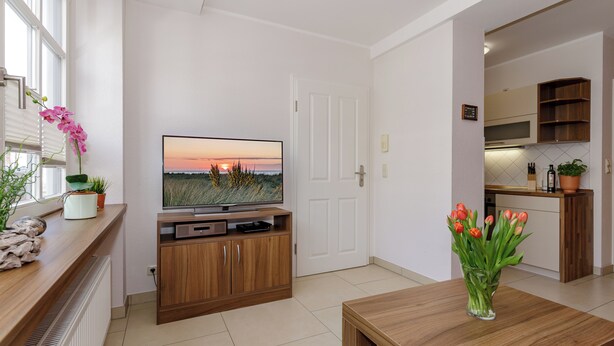 A modern living room with a television, wooden entertainment unit, a dining table, and a vase of flowers. - Apartment Elli 02 (Rostock)