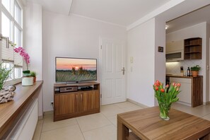 A modern living room with a television, wooden entertainment unit, a dining table, and a vase of flowers. - Apartment Elli 02 (Rostock)