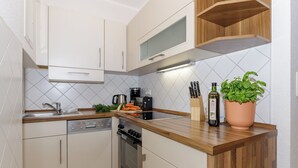 A modern kitchen with white cabinets, a wooden countertop, a dishwasher, an oven, and a potted basil plant. - Apartment Elli 02 (Rostock)