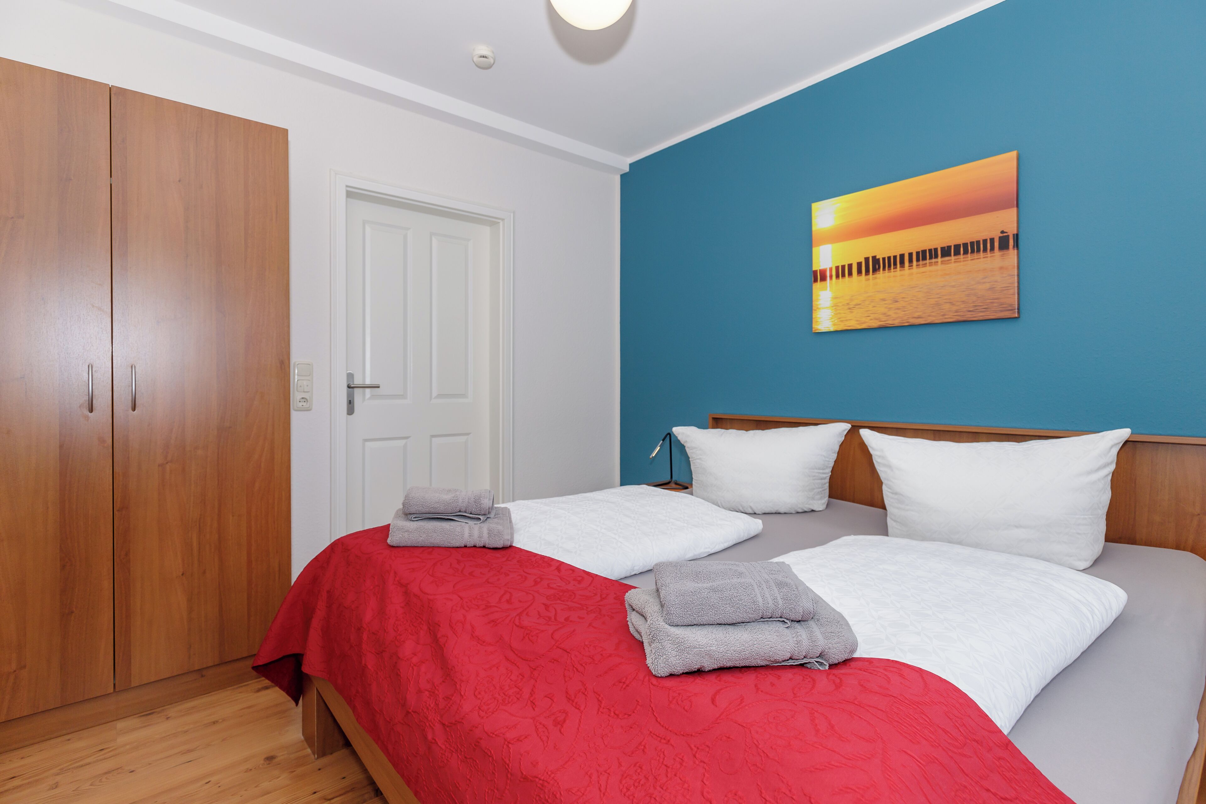 A bedroom with two beds, a wardrobe, a door, and a sunset painting on the wall.