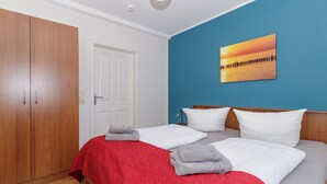 A bedroom with two beds, a wardrobe, a door, and a sunset painting on the wall. - Apartment Elli 02 (Rostock)