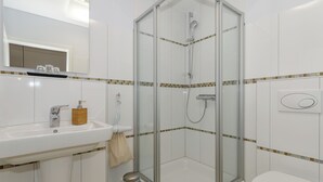 A bathroom with a glass-enclosed shower, a sink with a mirror, and a toilet. - Apartment Elli 02 (Rostock)