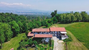 A large, two-story house with a red-tiled roof, surrounded by lush greenery and a view of distant mountains. - Green retreat with sauna and terrace: authentic mini apartment in Magnano (Piemonte)