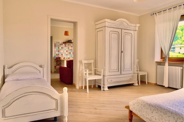 A bedroom with a bed, a wardrobe, a chair, and a view of a garden.