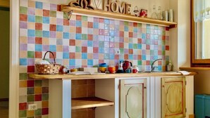 A kitchen with a colorful mosaic backsplash, wooden cabinets, and a shelf with kitchen items. - Green retreat with sauna and terrace: authentic mini apartment in Magnano (Piemonte)