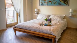 A bedroom with a wooden bed, floral bedding, a painting of birds, and bedside lamps. - Green retreat with sauna and terrace: authentic mini apartment in Magnano (Piemonte)